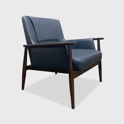 The Landon Lounge Chair from Jamie Stern features a tight upholstered back with a head rest cover, an exposed wood frame and round tapered legs.